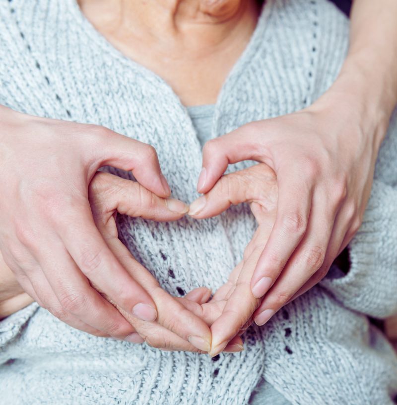 zwei Händepaare formen ein Herz. Das innere Händepaar ist von einer älteren Dame