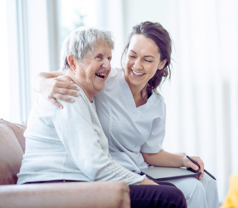 Pflegerin umarmt ältere Dame und beide lachen fröhlich
